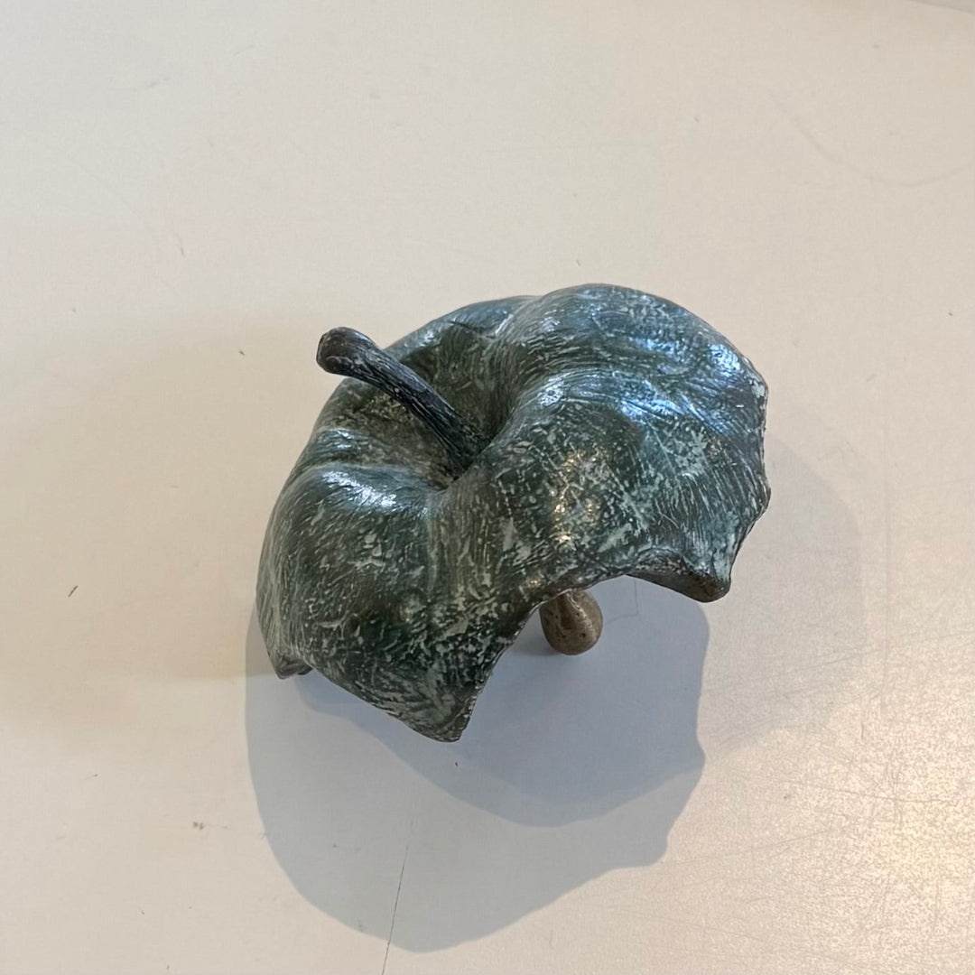 Greenish-brown cast bronze half eaten apple sculpture on a beige background