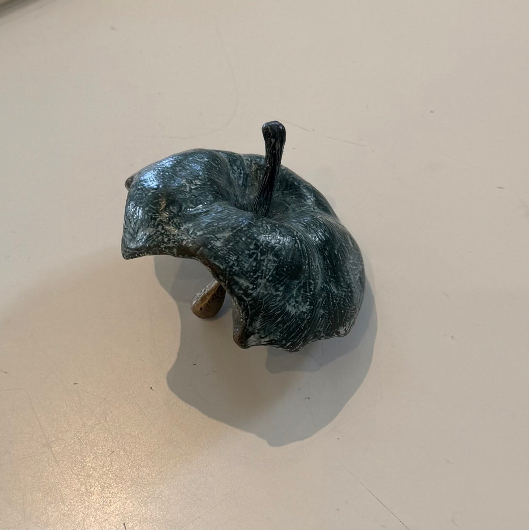 Greenish-brown cast bronze half eaten apple sculpture on a beige background