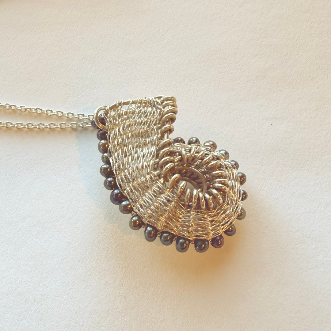 Silver wire-wrapped pendant with blue pearls on a light background