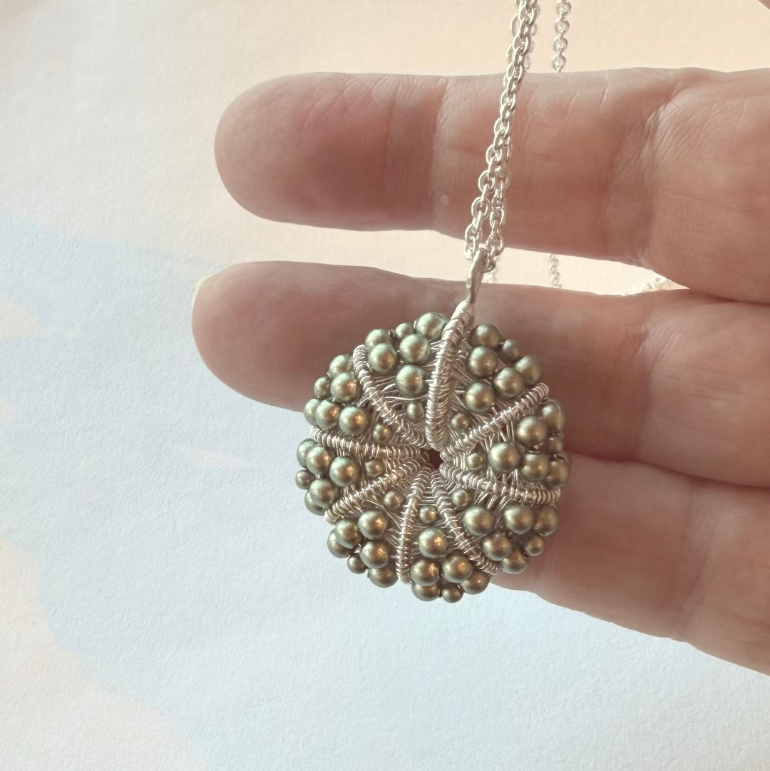 Hand holding a silver necklace with a textured pendant against a light background