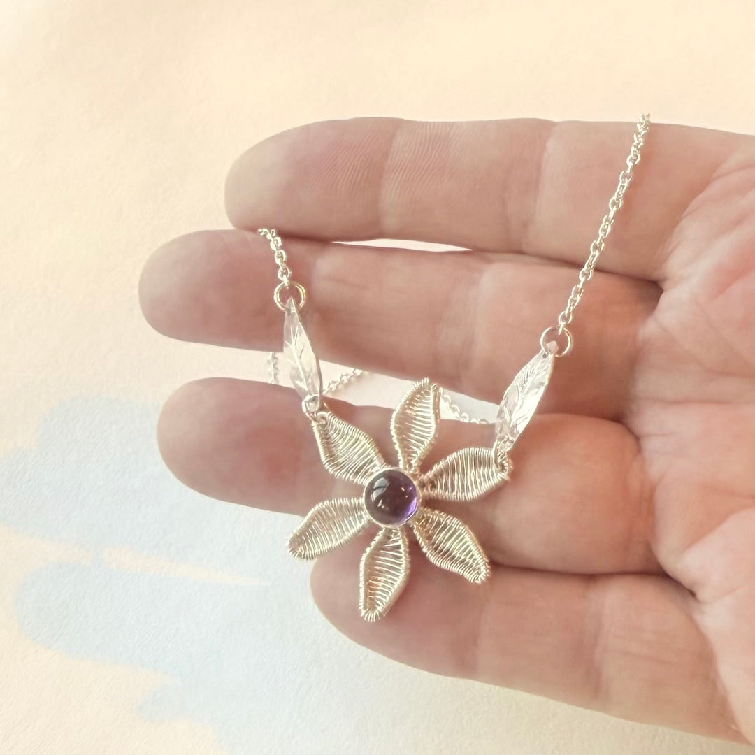 Delicate silver necklace with a floral design held in a hand against a soft background