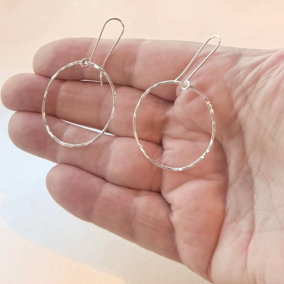 Silver hoop earrings held in a hand against a light background