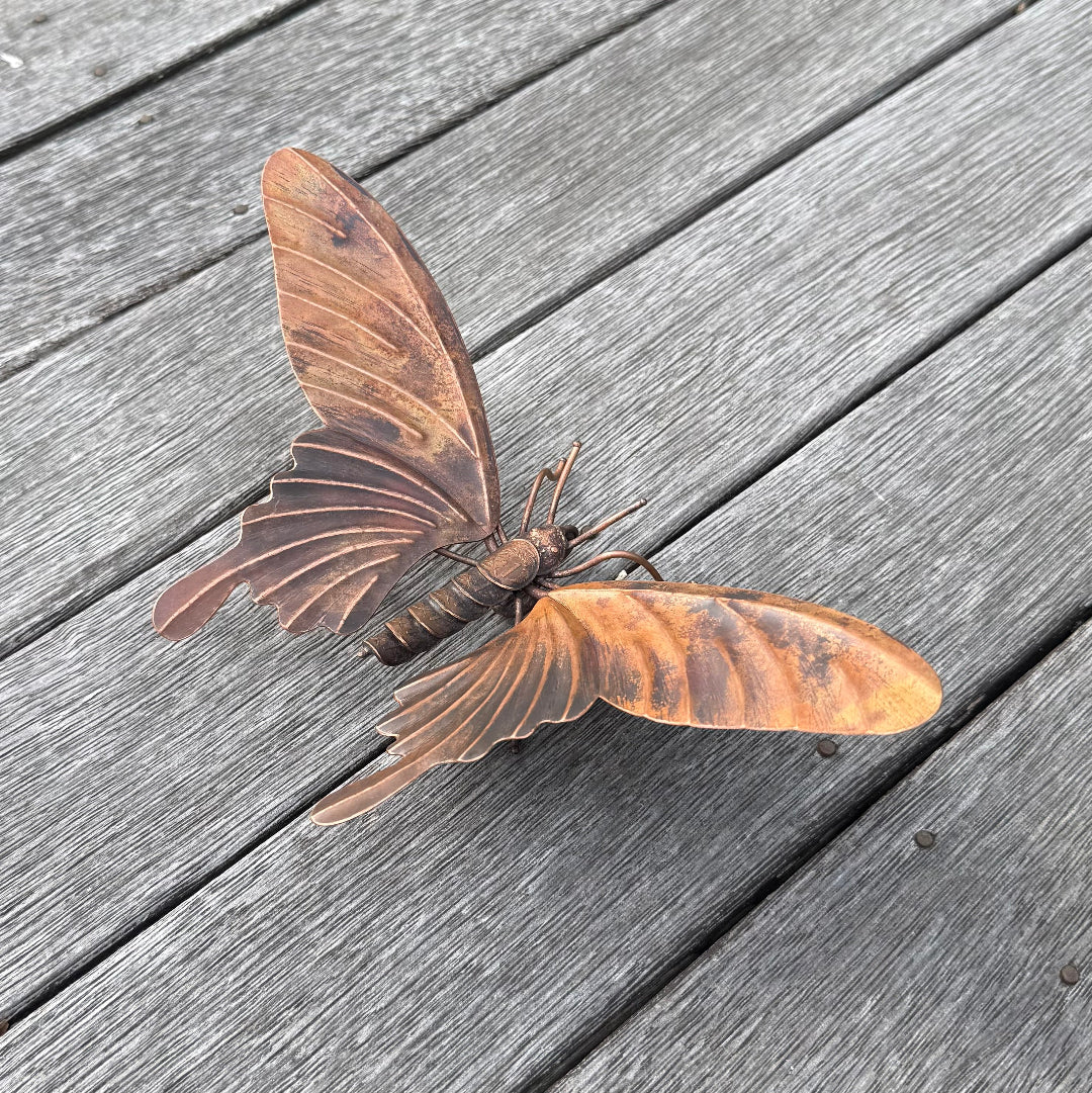 Copper butterfly sculpture with coin body on a wooden surface