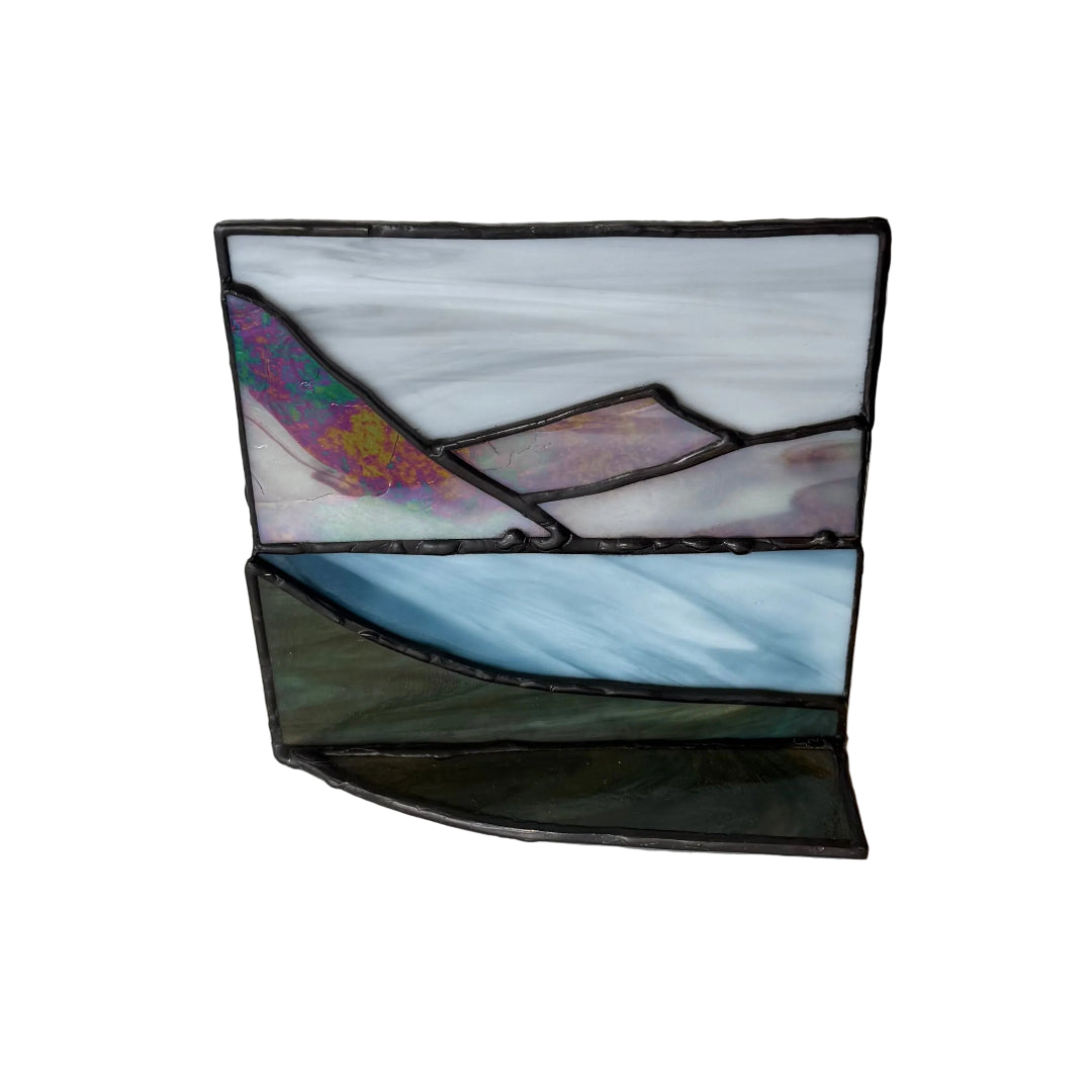 A small stained glass art piece depicting a landscape with a white and blue sky, a purple mountain, and a dark green foreground, outlined in black metal.