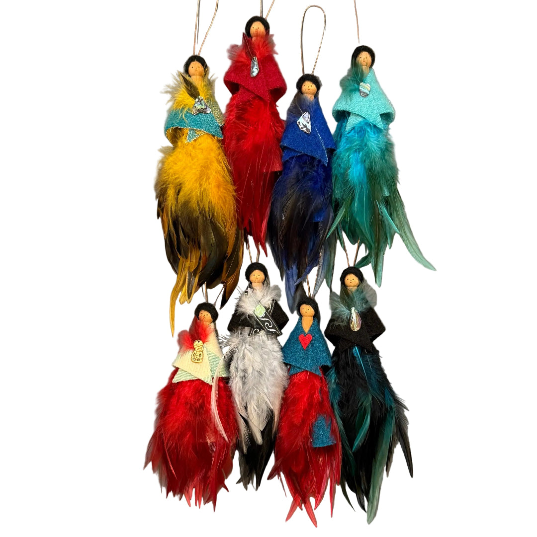 Eight handmade peg doll ornaments hanging from copper wire against a white wall. Each ornament features a small fabric figure with black hair and a colorful feathered dress in various colors including yellow, red, blue, teal, white, and black.