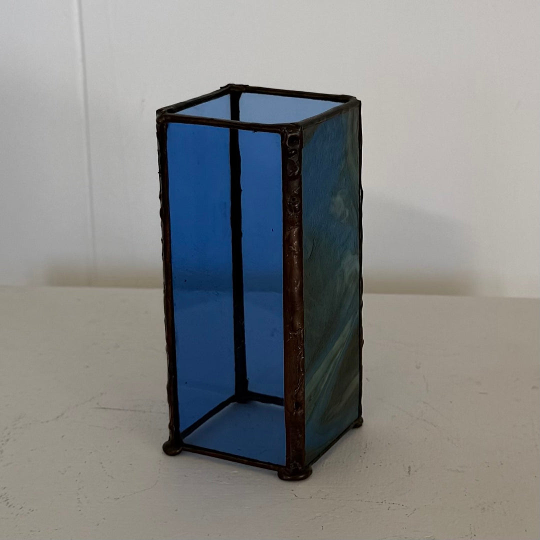 A rectangular vintage stained glass vase with cobalt blue glass panels and a dark, rustic wrought-iron frame, set against a plain off-white background.