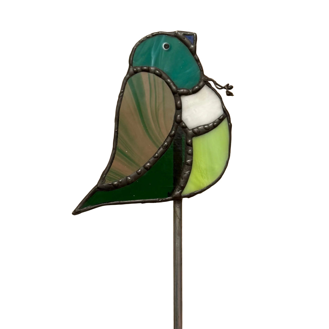 A stained glass bird figurine on a metal stake, featuring green, white, and light yellow-green glass panels with dark metal outlines, set against a white background.