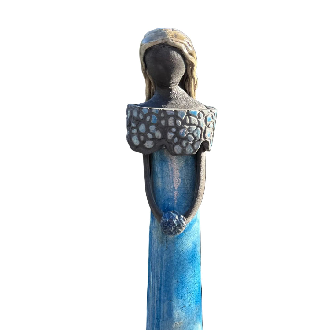 A decorative figurine of a woman with a long blue skirt and patterned top, on a white background.