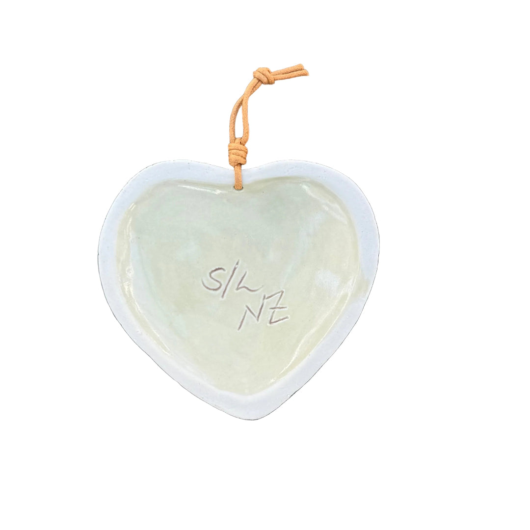 Back view of a heart-shaped ceramic wall hanging ornament with a white rim and a pale green glazed center, signed S/L NZ.