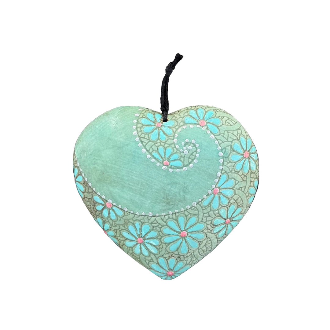 A heart-shaped ceramic wall hanging ornament with a spiral & daisy design in  green, cream, and blue, hanging on a white wall.