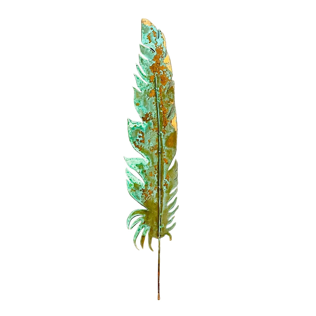 A decorative copper feather wall art piece with a distressed patina showing green verdigris and orange rust-like oxidation, mounted on a white wall.