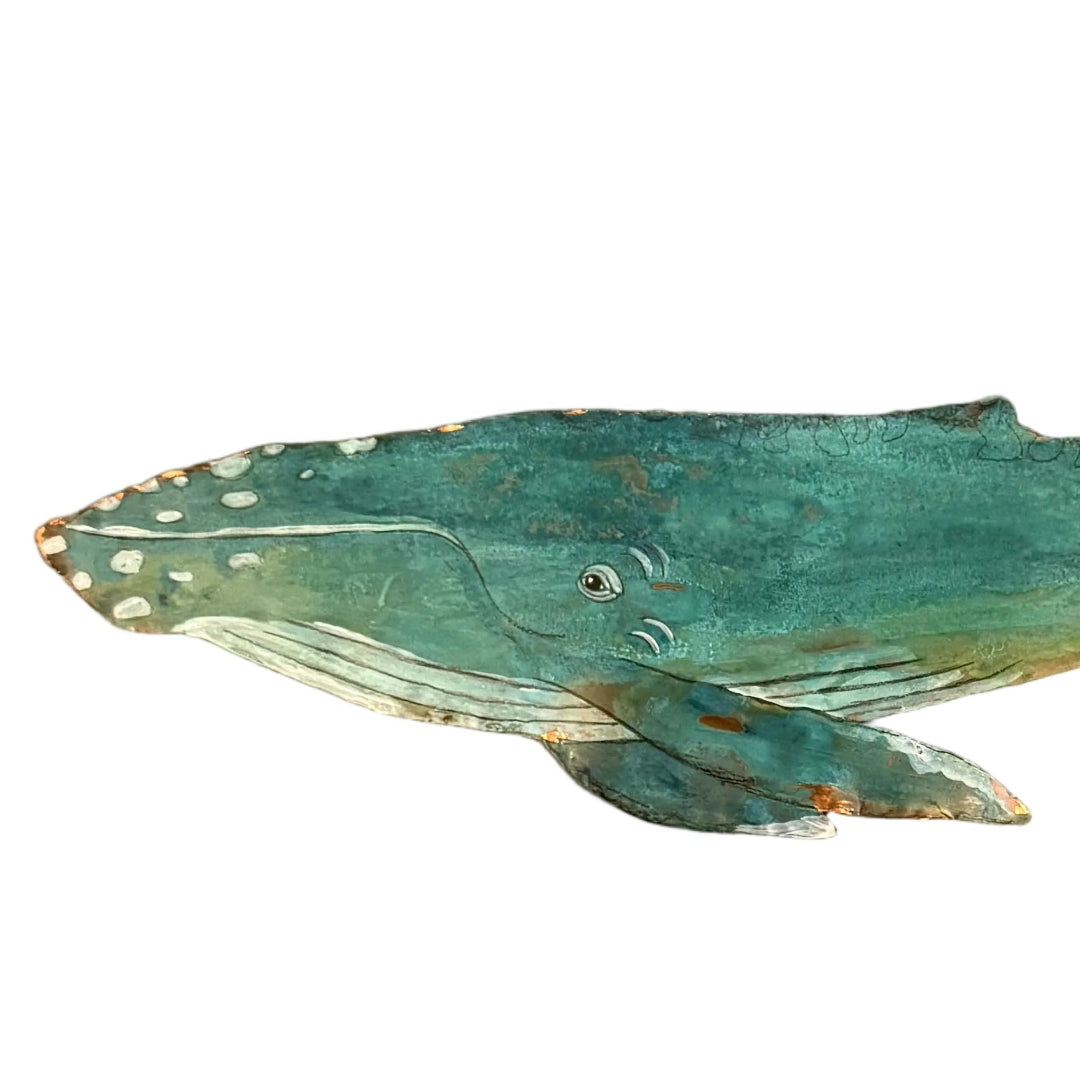 A close up view of a copper whale wall art piece with a textured, weathered finish in shades of teal, green, and brown, mounted on a white wall.