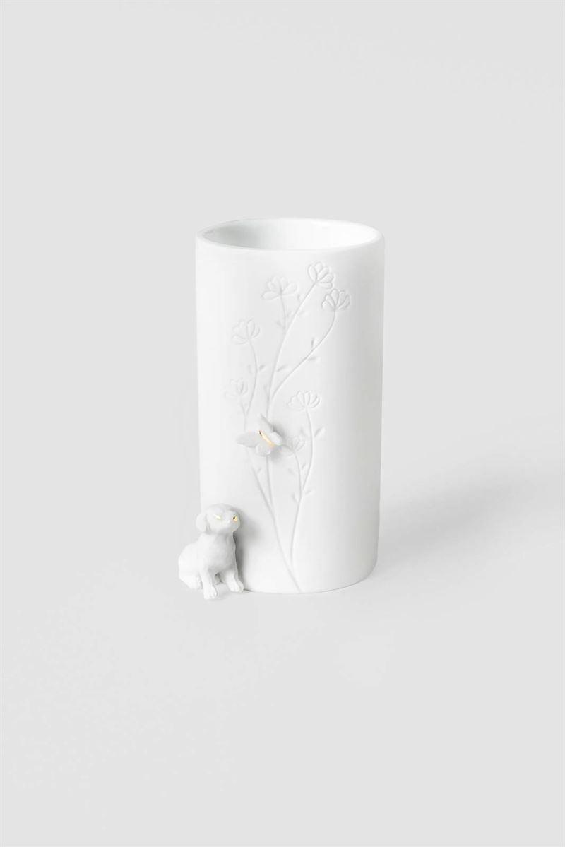 A white ceramic cylindrical vase with a delicate embossed floral branch design and a small dog figurine watching a butterfly at the base, shown on a clean light gray background.