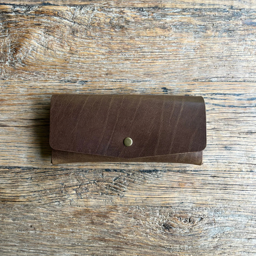Brown leather glasses case with a gold button on a wooden surface