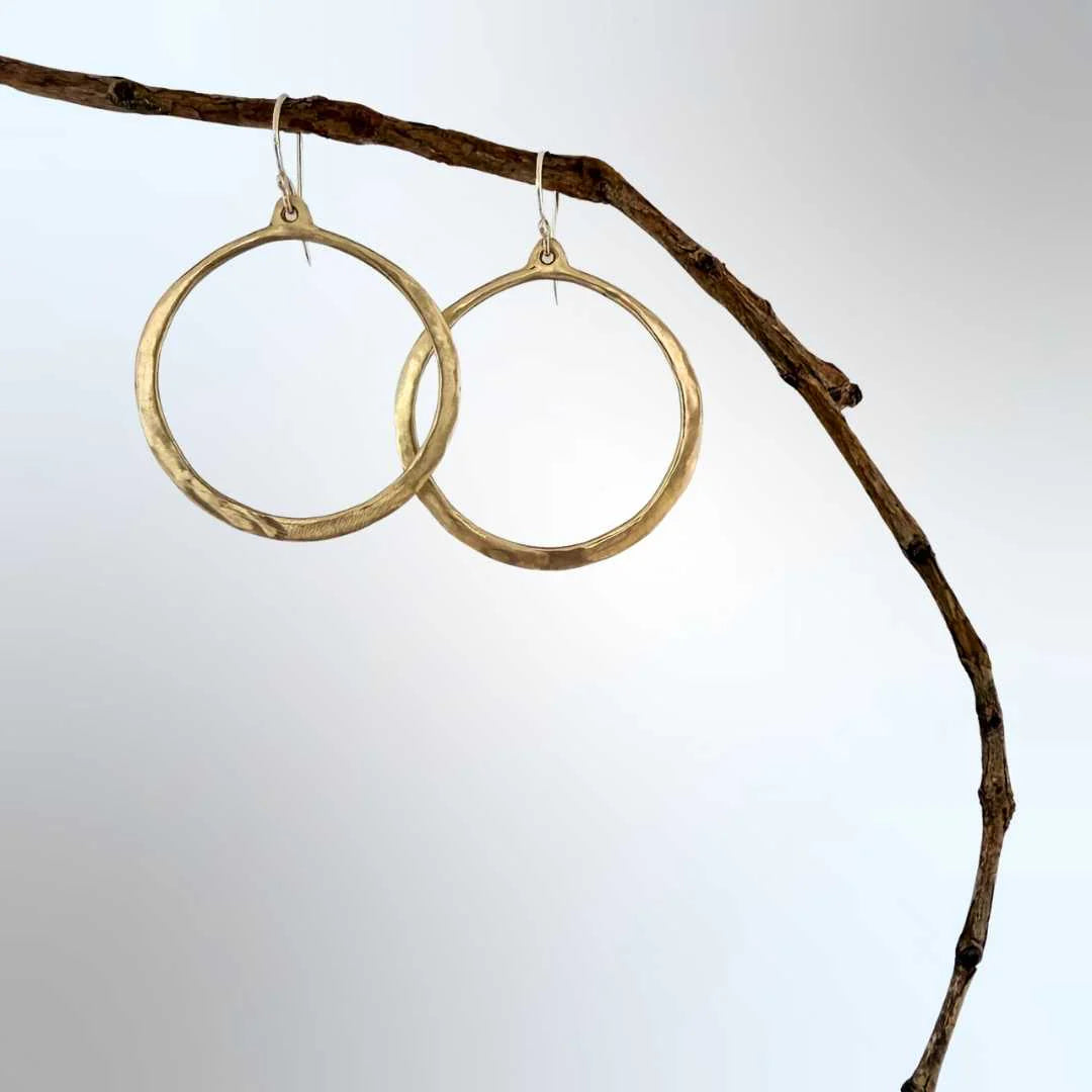 Bronze hoop earrings hanging from a branch against a light background