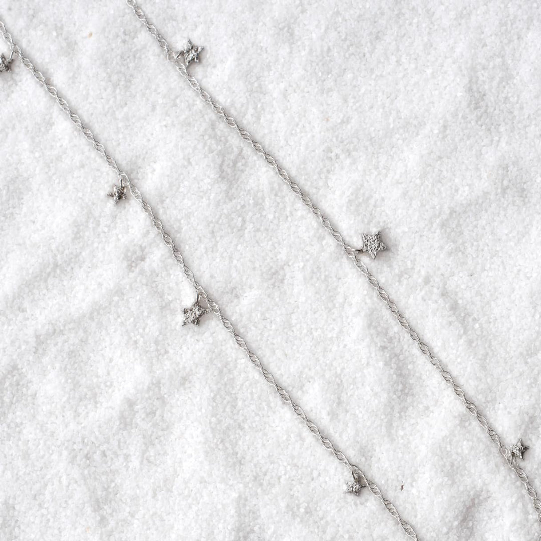 Silver necklace with small star pendants on a textured white surface