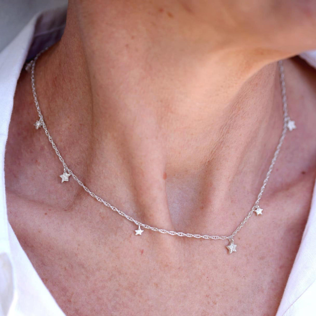 Silver necklace with star pendants on a person wearing a white shirt.