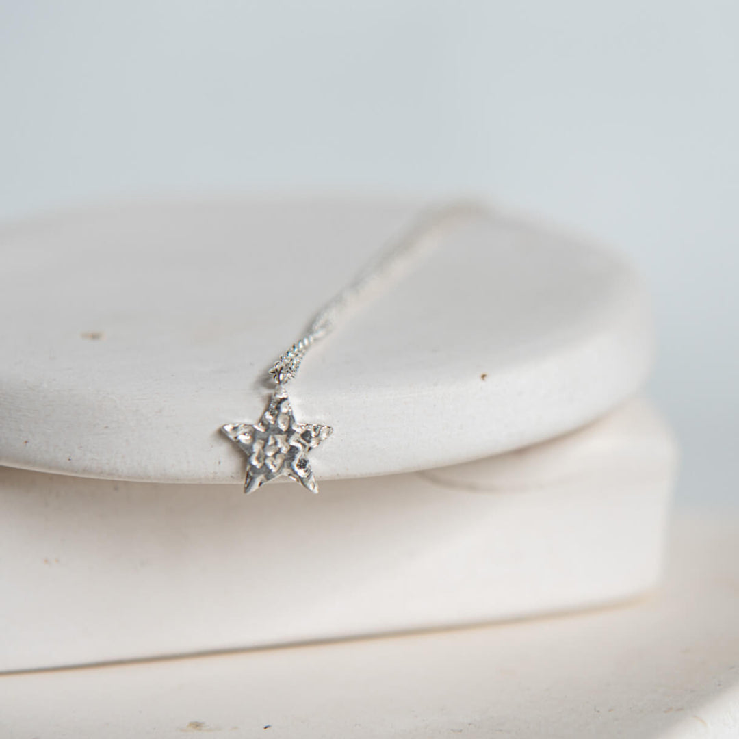 Silver star-shaped pendant on a chain against a white background
