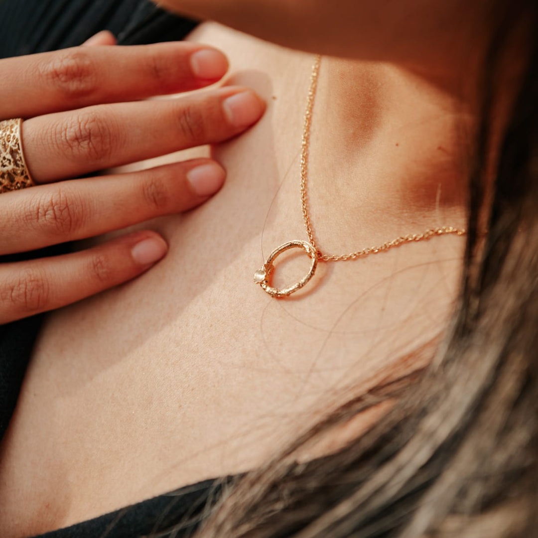 Close-up of a person wearing a delicate gold necklace with a circular pendant.