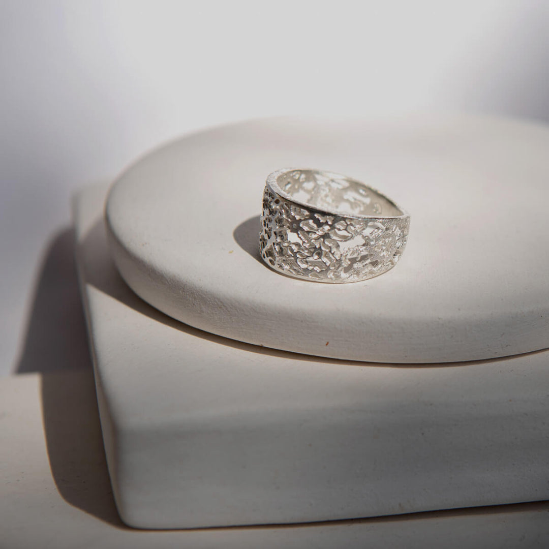 Silver ring with textured design on a white stand