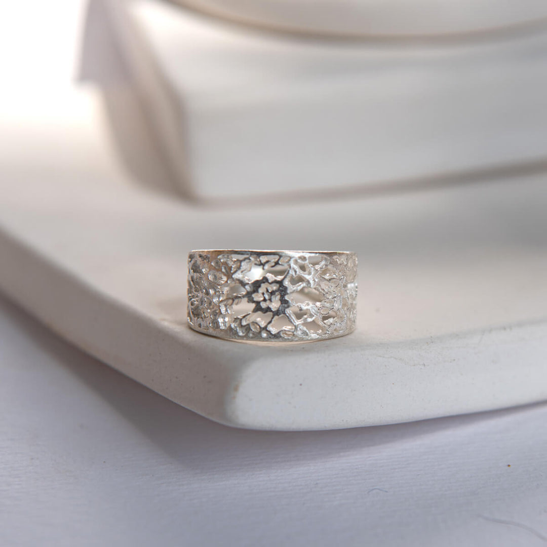Silver ring with a textured lace design on a white ceramic plate