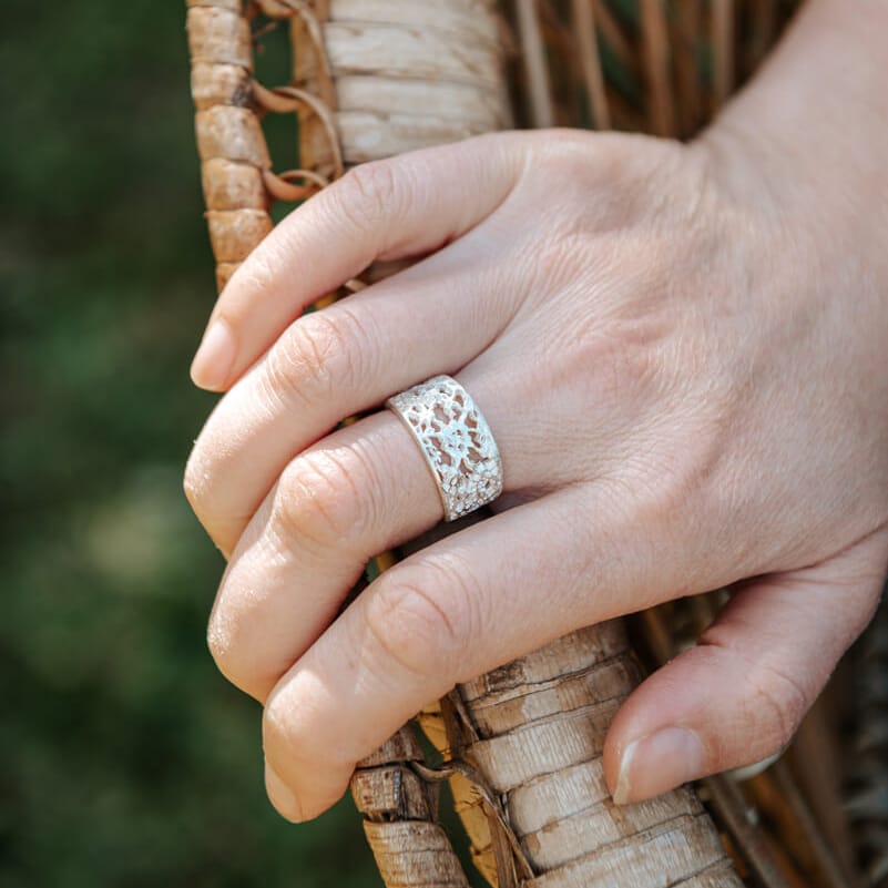 Hand wearing a silver ring holding a woven basket with a blurred green background