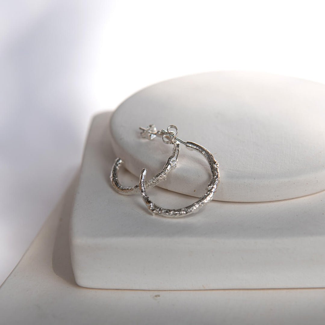Silver hoop earrings on a white surface with a soft light background