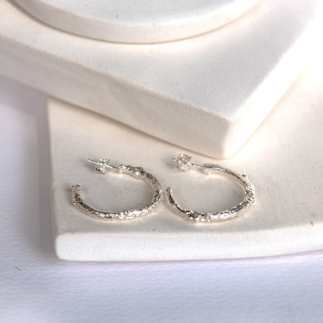Silver hoop earrings on a white stone surface