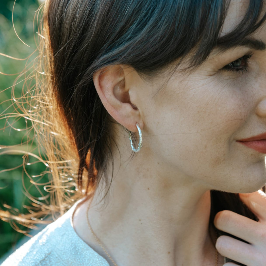 Close-up of a woman wearing silver hoop earrings with a blurred green background