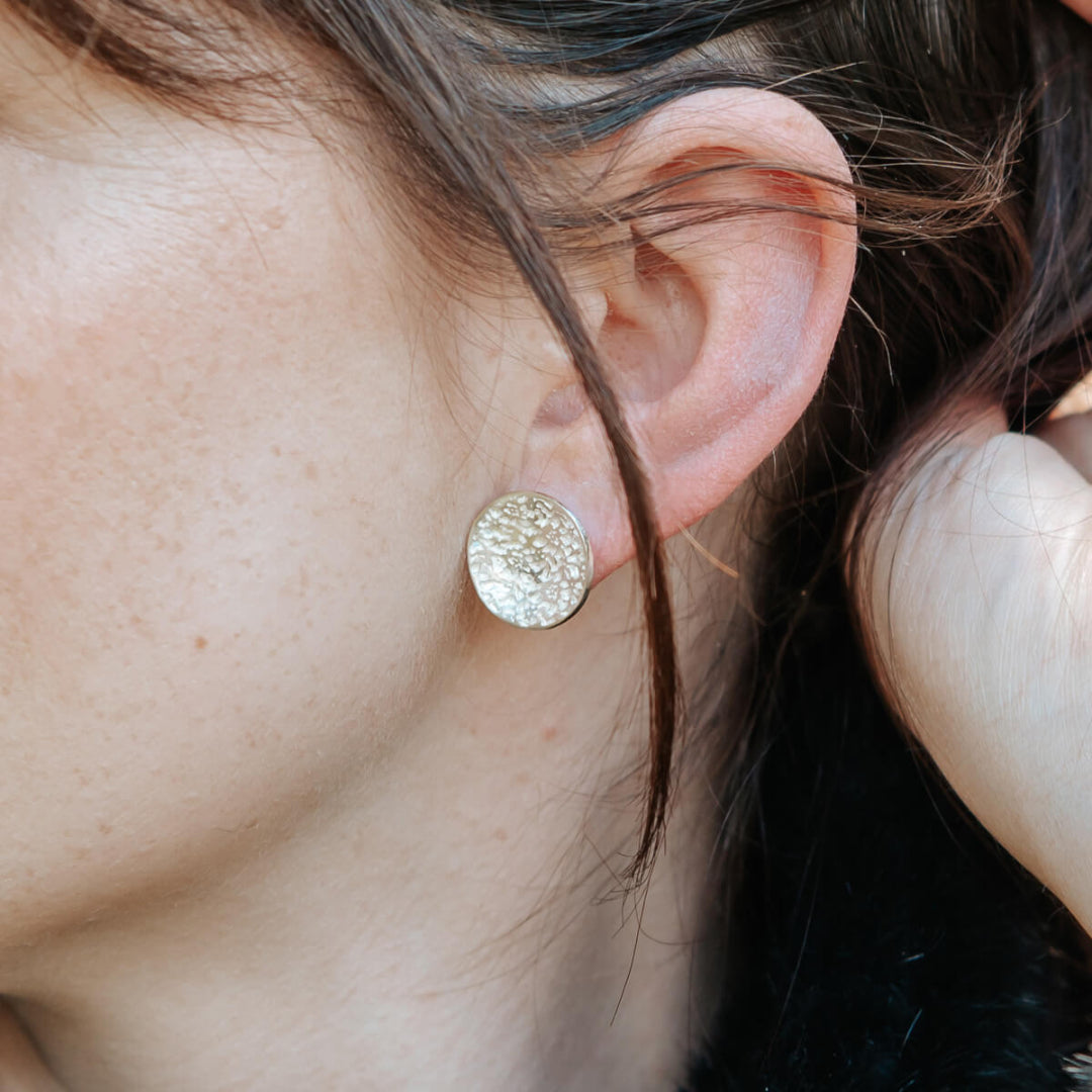 Close-up of a person wearing silver round earrings.