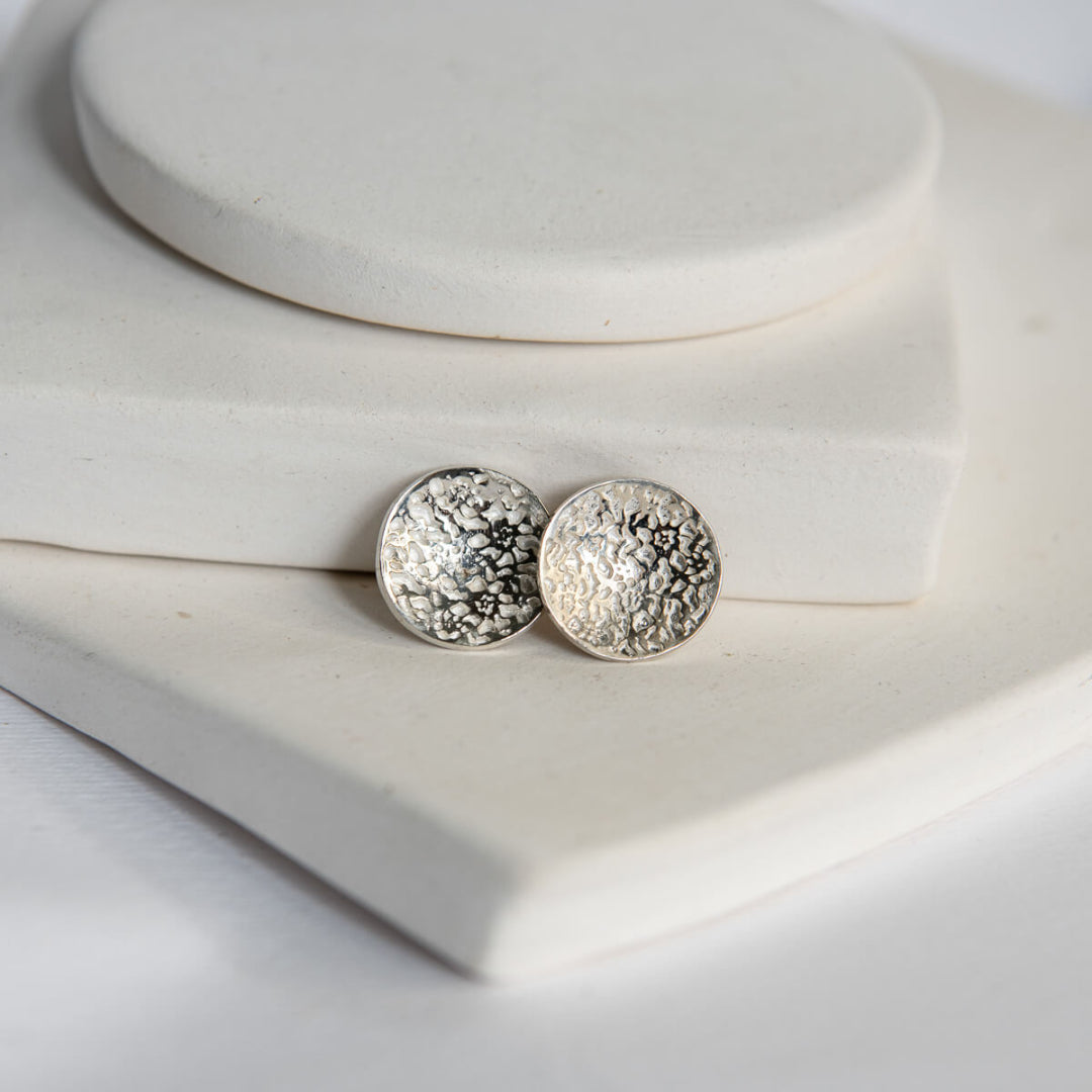 Silver round textured earrings on a white jewelry display