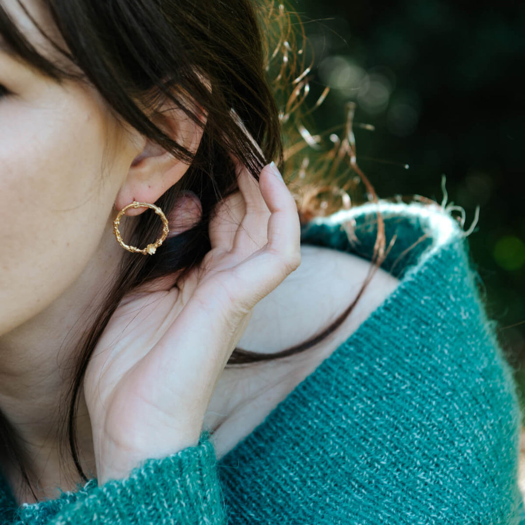 Close-up of a person wearing a gold hoop earring with a blurred natural background