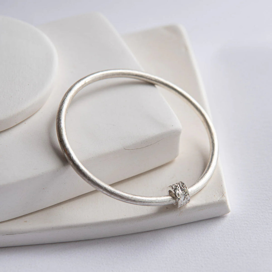 Silver bracelet with a small decorative element on a white surface