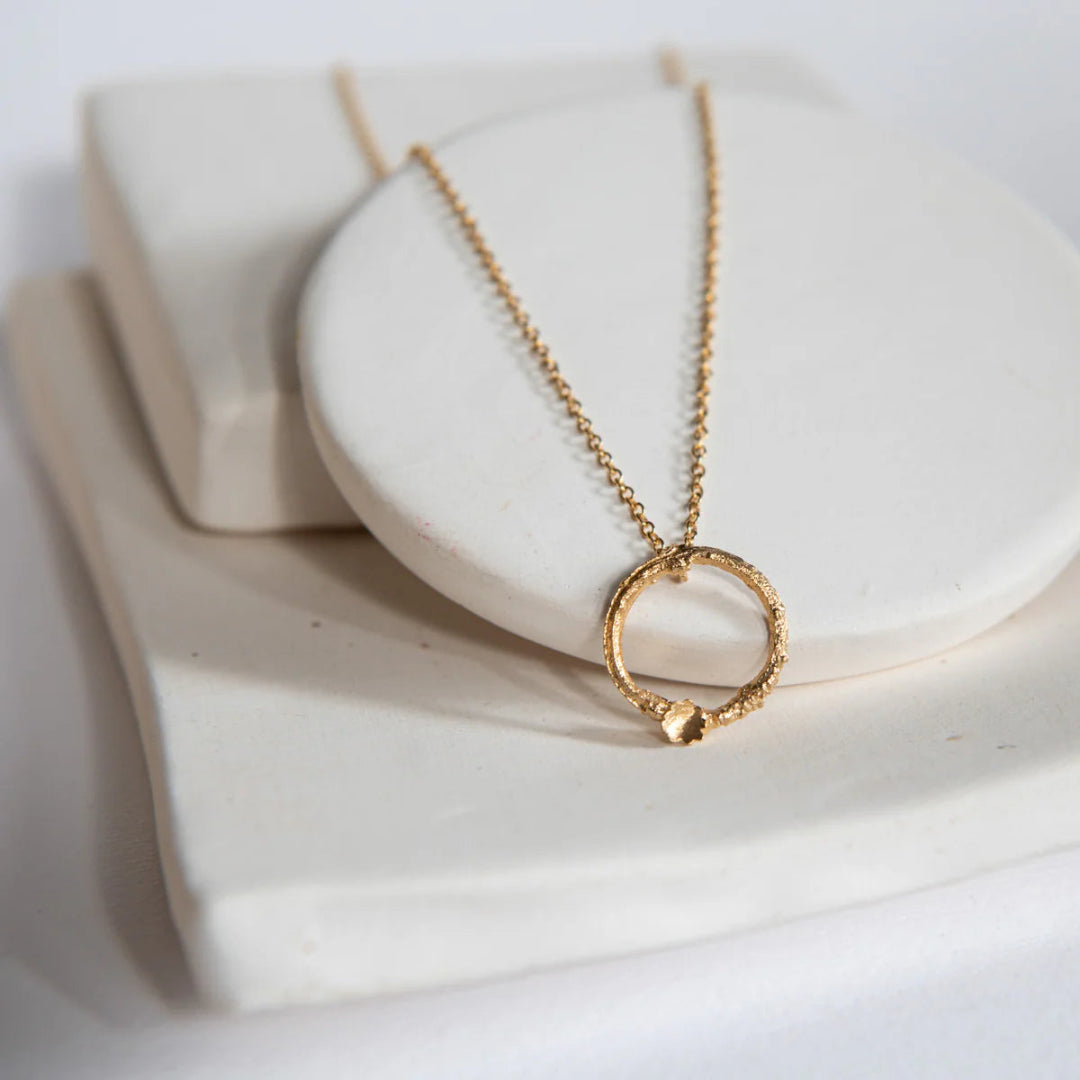 Gold necklace with a circular pendant on a white surface