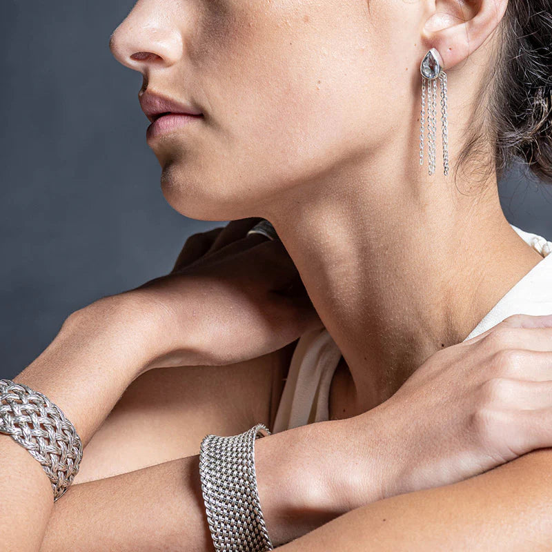 Close-up of a person wearing silver earrings and bracelets against a neutral background