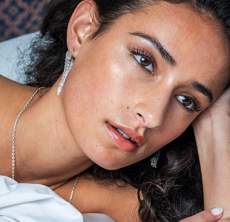 Close-up of a woman with silver jewelry and white top, lying on a textured surface.
