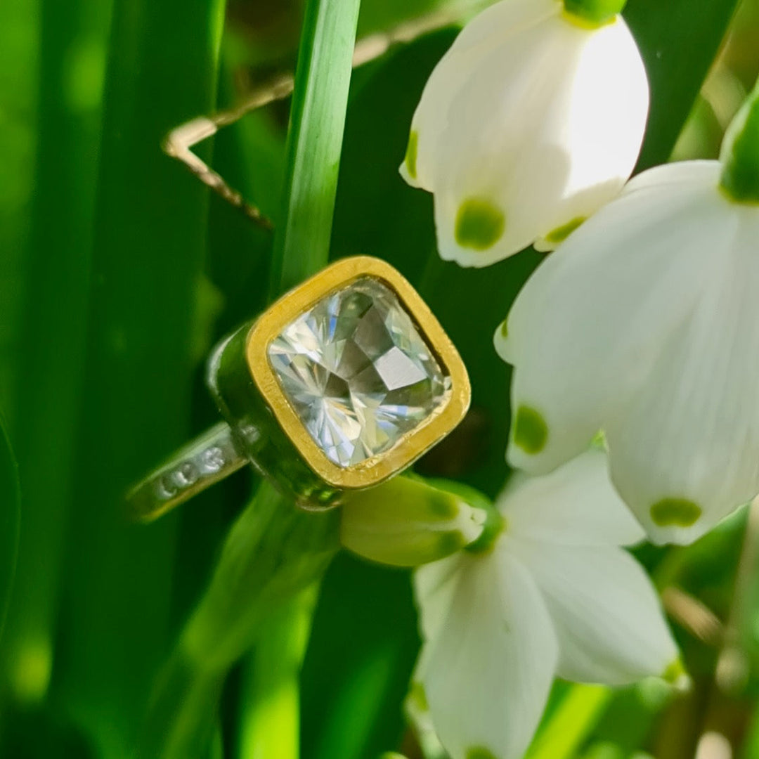 Gold & silver ring with a clear topaz gemstone on a background of white flowers and green leaves