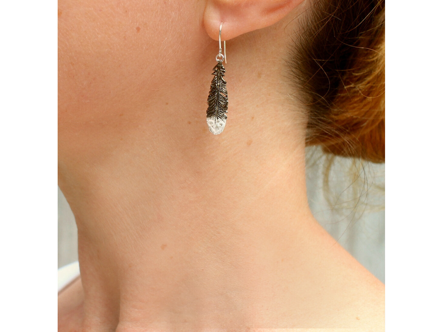 Side view of a person wearing a black & white painted silver Huia feather earring 