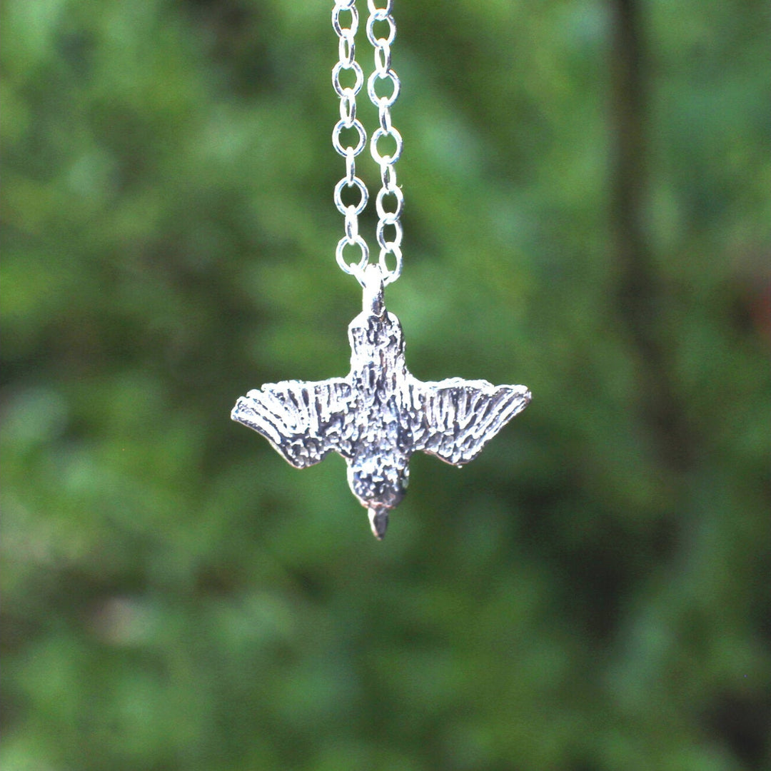Shiny Silver Diving Kingfisher pendant on a chain against a blurred green background