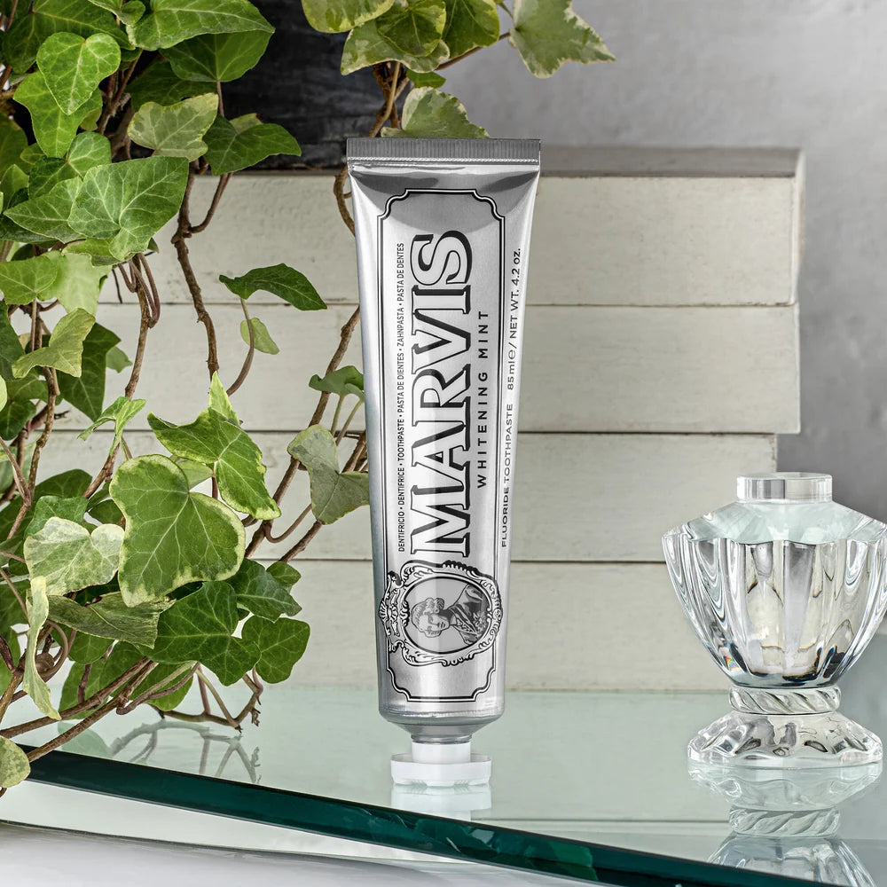 Marvis toothpaste tube on a reflective surface with a plant and decorative item in the background