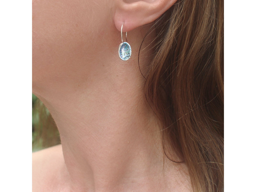 Side view close-up of a person wearing a painted multicoloured silver Paua Shell earring.