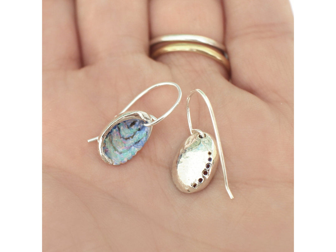 Painted multicoloured Paua Shell Silver earrings held in a hand