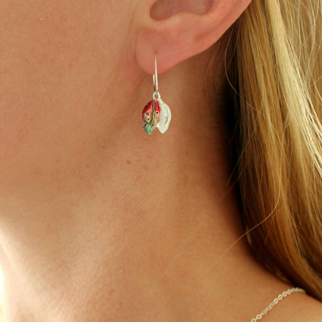 Close-up of a person wearing a red & green hand painted on silver leaf earring.
